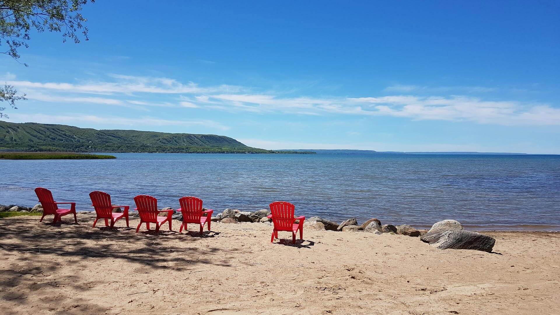 Red Muskoka chairs on the private Georgian Bay beach for Tyrolean guests near Collingwood
